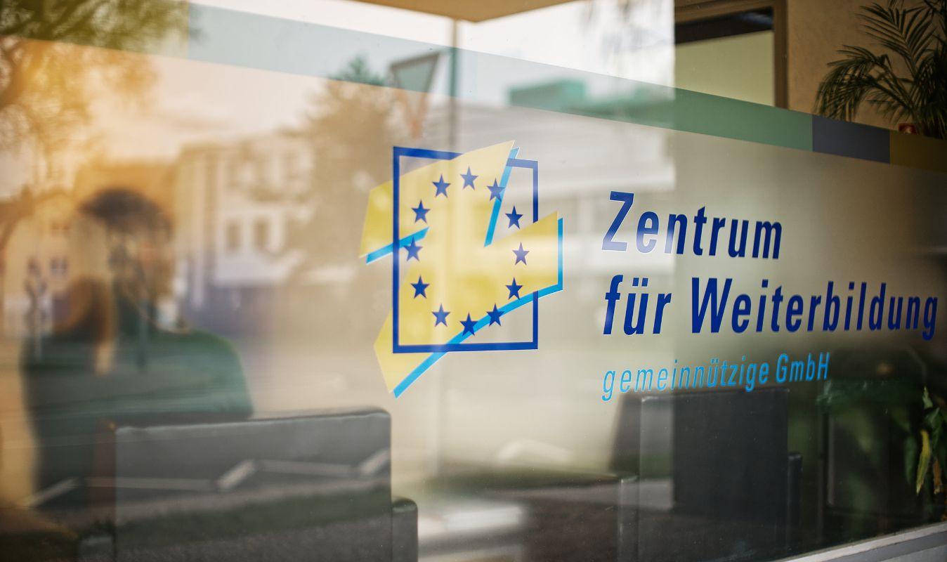 Logo des Zentrum für Weiterbildung auf einer Glastür mit Straßenreflexion