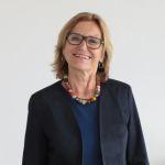Portrait Barbara Wagner - Frau mit blonden Haaren und Brille, trägt dunklen Blazer und buntem Halsschmuck, vor hellem Hintergrund