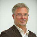 Portrait Markus Schumacher - Mann mit grauen Haaren und Brille in braunem Jackett mit weißem Hemd