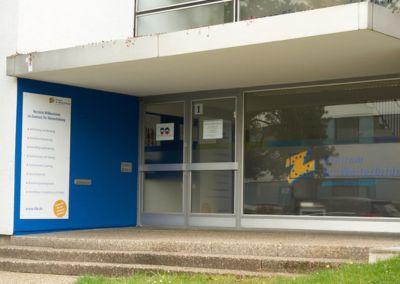 Zentrum für Weiterbildung – Standort Darmstadt Eingangsbereich des Standorts Darmstadt des Zentrums für Weiterbildung mit blauer Tür und großem Fenster mit Logoaufschrift.