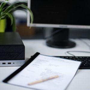 Arbeitsplatz mit Computer, Tastatur und einem Lebenslauf im Vordergrund auf dem Tisch.