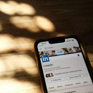 Smartphone zeigt LinkedIn-Profilseite auf einem hölzernen Tisch mit Lichteinfall.