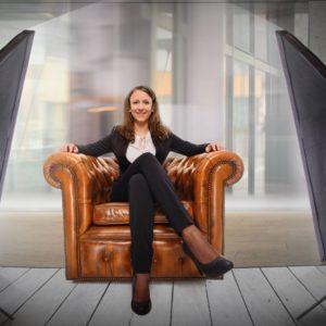Frau im Business-Outfit sitzt in einem Fotoshooting-Setting auf einem Ledersessel.