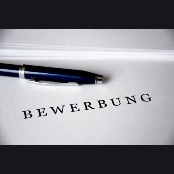 Nahaufnahme einer Bewerbungsmappe mit dem Titel „BEWERBUNG“ und Kugelschreiber auf weißem Tisch.