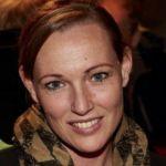 Kristin Achilles – Zentrum für Weiterbildung Kristin Achilles - Porträt einer lächelnden Frau mit zusammengebundenen Haaren und gemustertem Schal, aufgenommen in warmer Lichtstimmung.