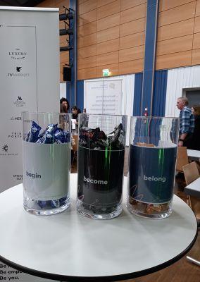 Drei transparente Behälter mit Süßigkeiten, beschriftet mit „begin“, „become“ und „belong“.