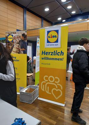 Lidl-Ausbildungsstand mit zwei Roll-Ups, einer Box und mehreren Jugendlichen.