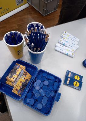 Tisch mit Lidl-Werbegeschenken wie Stiften, Chips, Linealen und Infoflyern.