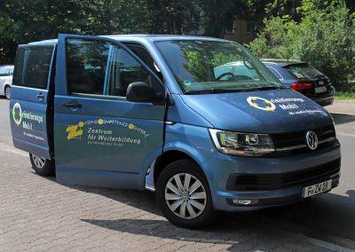 Blaues Fahrzeug mit der Aufschrift „Orientierungsmobil – Zentrum für Weiterbildung“ steht mit offener Seitentür am Straßenrand, im Hintergrund grüne Bäume und parkende Autos.