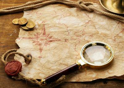 Alte Schatzkarte auf Holztisch mit Lupe, Kompassrose, Münzen, Seil und Wachssiegel.